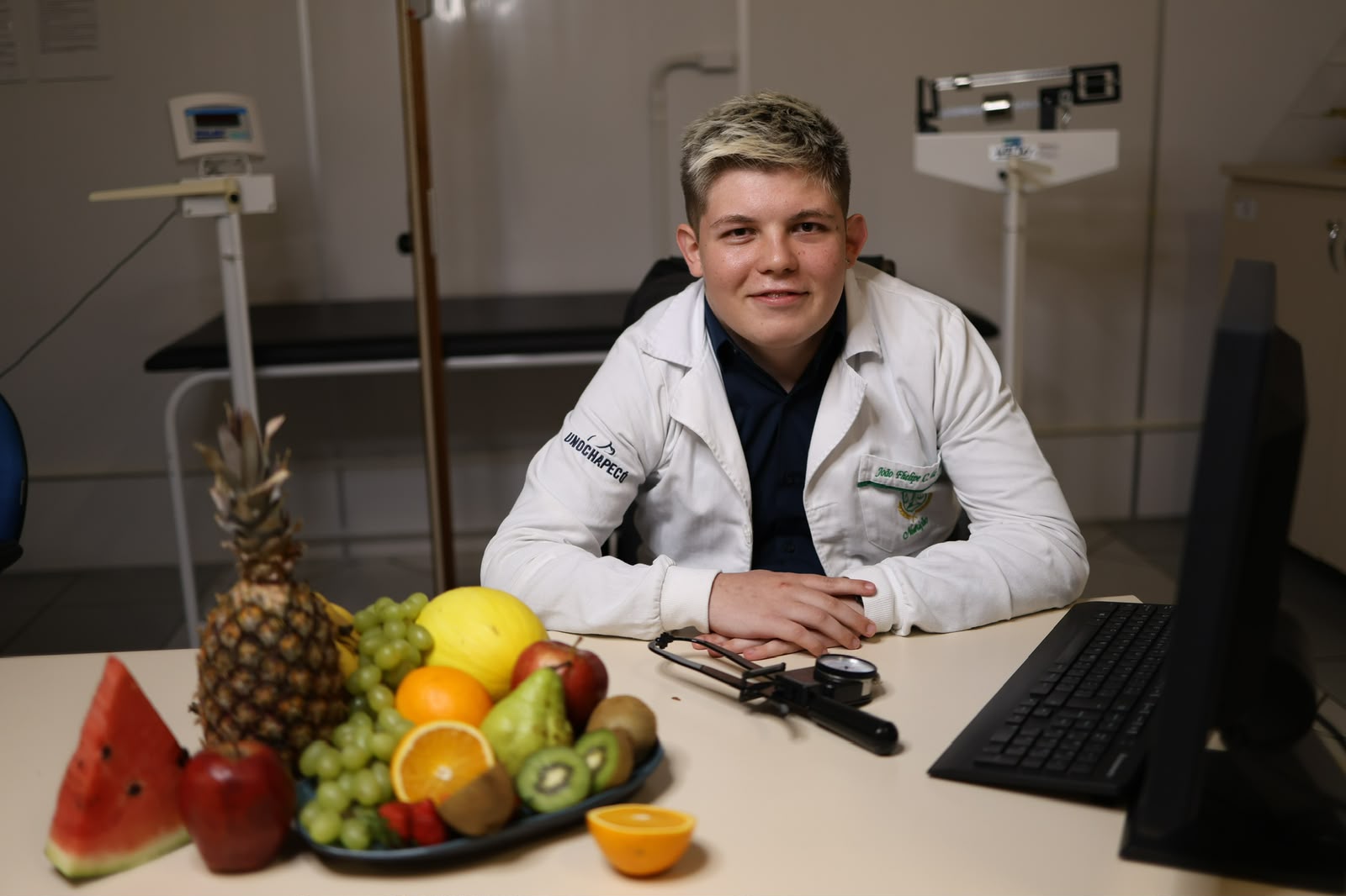 Nutricionista em Chapeco, Joao Fhelipe, sentado no consultorio com frutas na mesa durante avaliacao nutricional